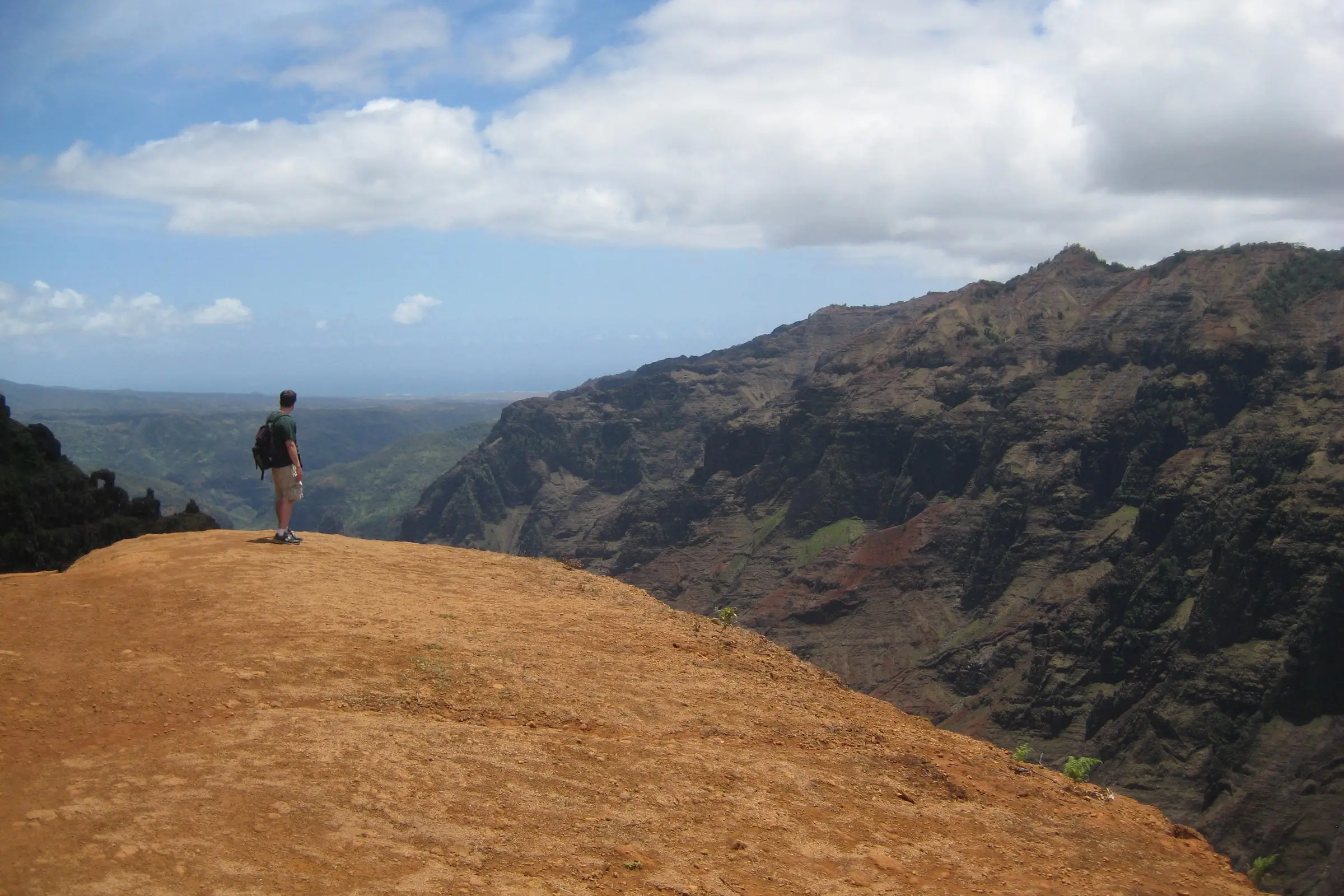 hiker standing at the edge of a red dirt cliff above a canyon