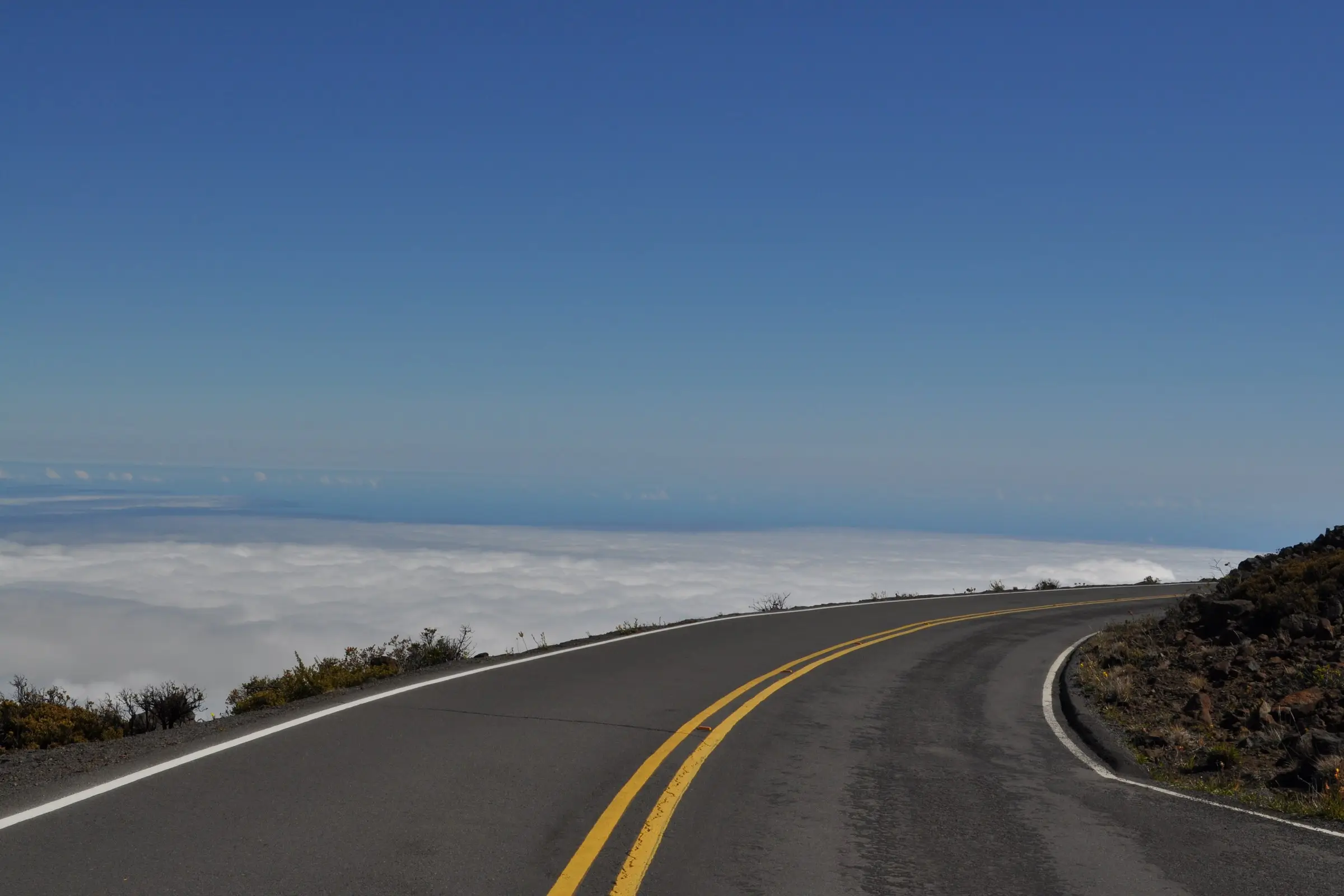 an empty mountain road curving above the clouds