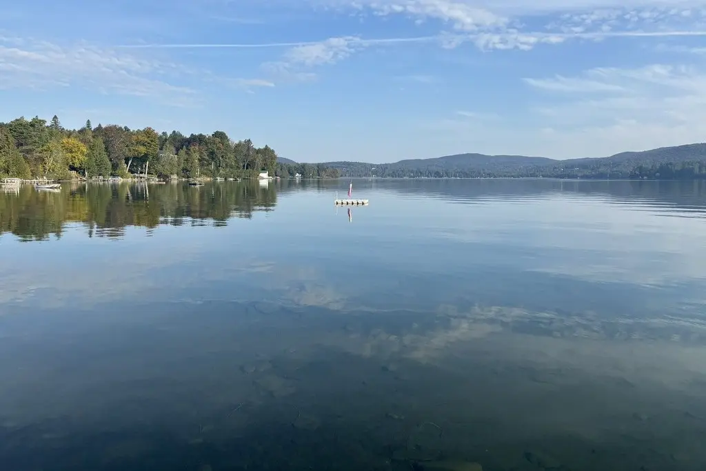a still lake reflecting a blue morning sky and a wooded shore
