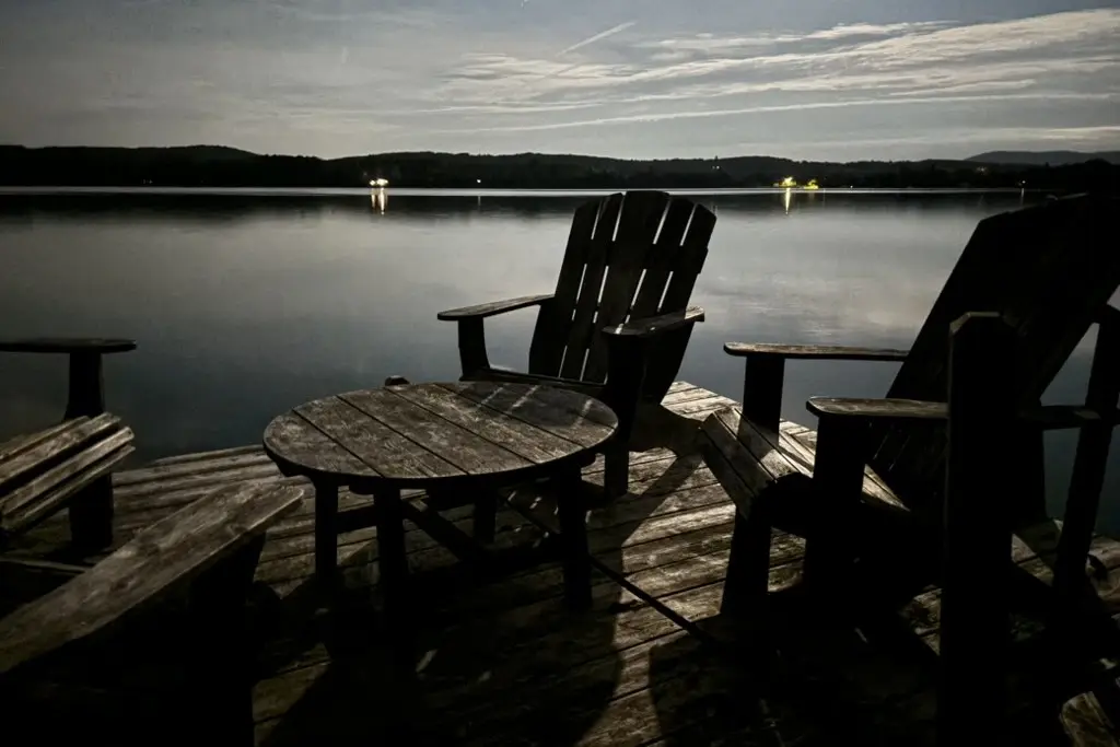 two wooden chairs and a table on a lakeside dock at dusk