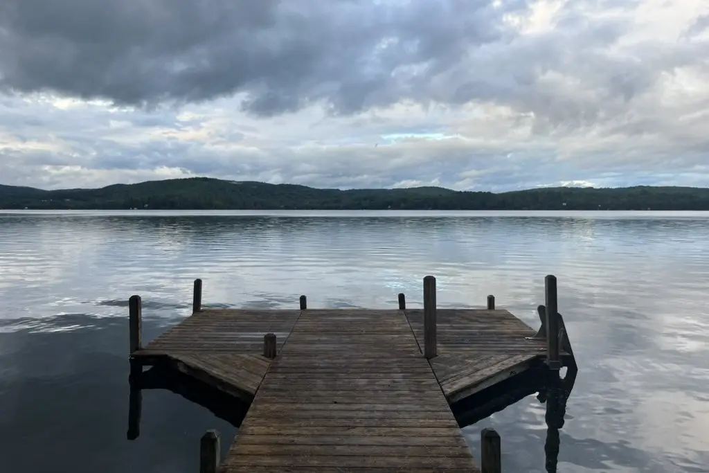 a wooden dock reaching into a calm lake under gray clouds