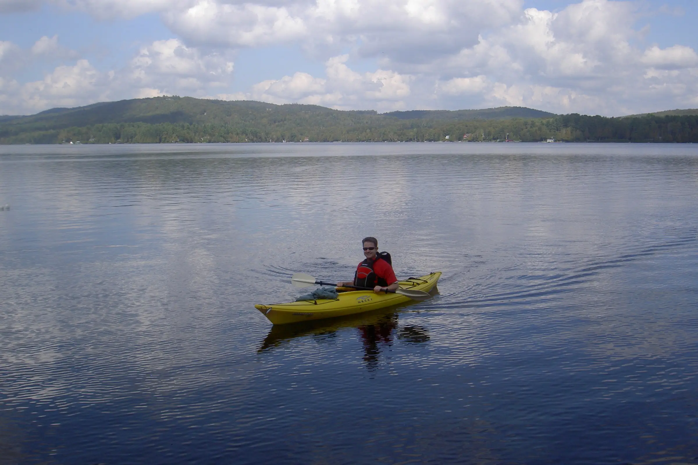 man paddling a yellow kayak on a calm lake